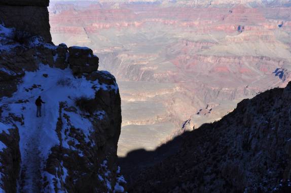 Início de caminhada, a trilha ainda na sombra enquanto, ao fundo, o sol inunda o Grand Canyon no Arizona, nos Estados Unidos